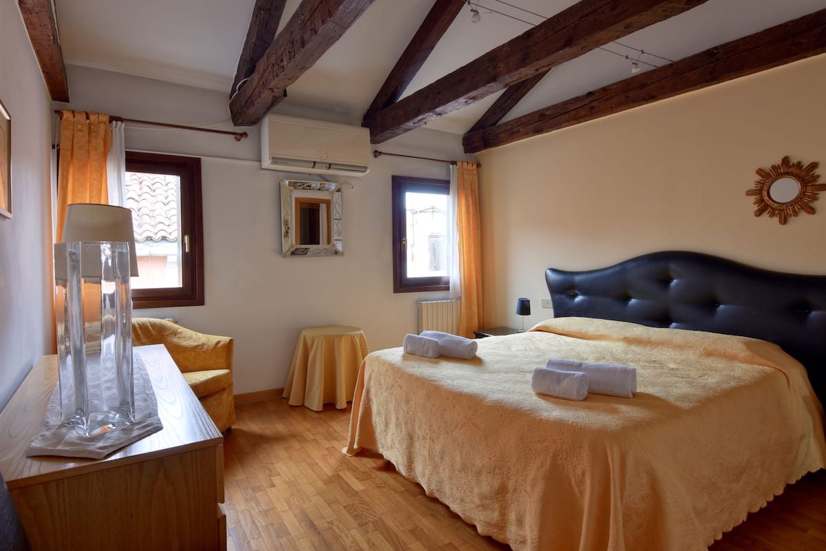 A bedroom with a large bed, wooden beams, a small table, and a mirror.