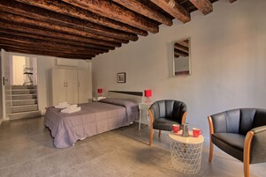 Una camera da letto con un letto, due sedie, un tavolino, uno specchio e una scala che conduce a un'altra stanza.