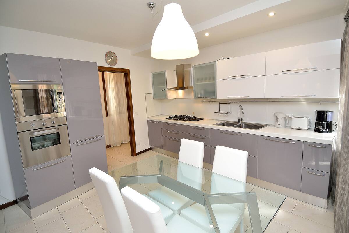 A modern kitchen with stainless steel appliances, a glass dining table, and white cabinetry.