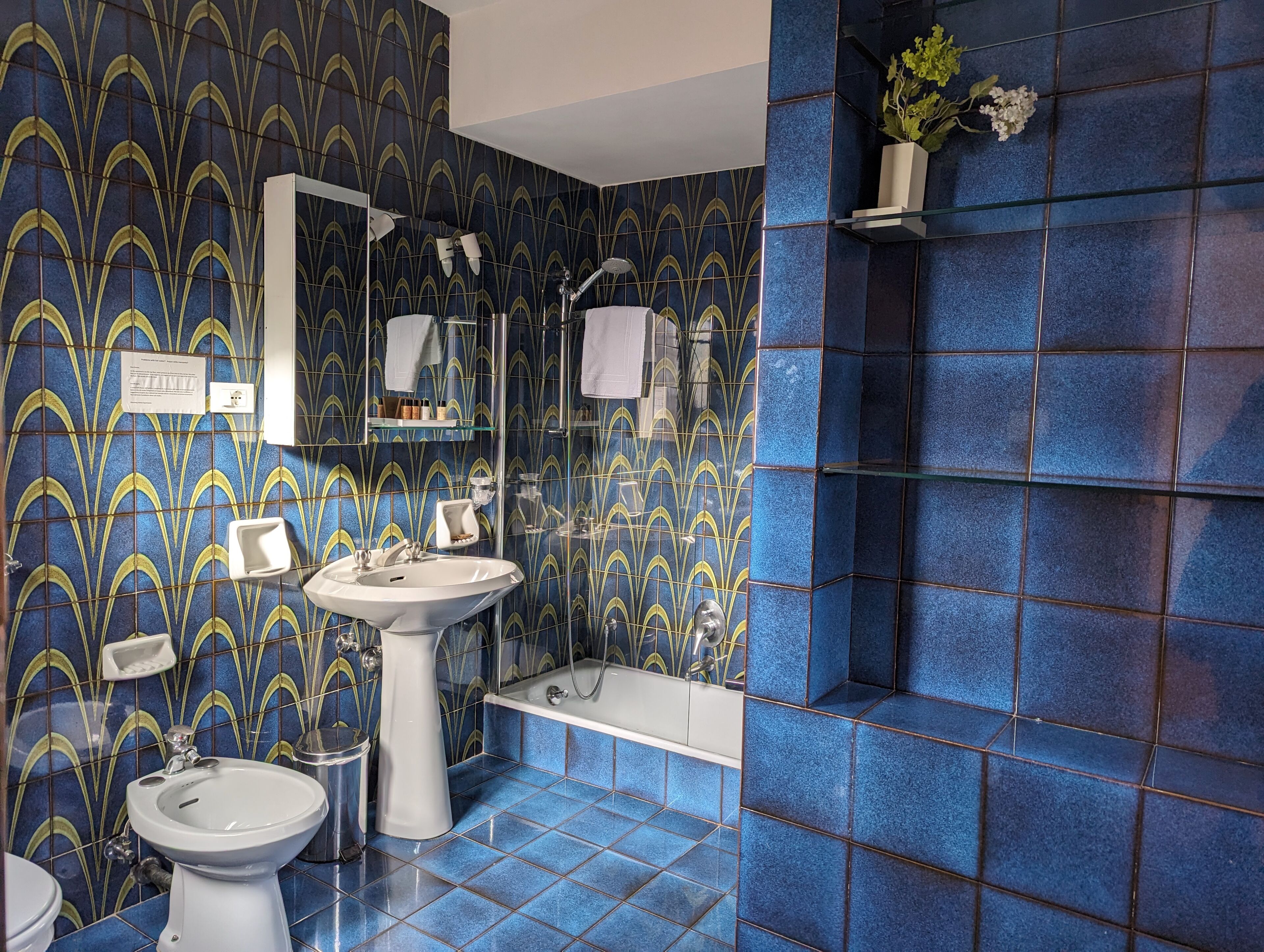 A bathroom with a blue and yellow patterned tile wall, a white sink, a bidet, and a bathtub.