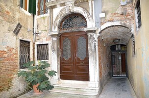 Un vicolo stretto con un'imponente porta in legno decorata e una pianta in vaso.