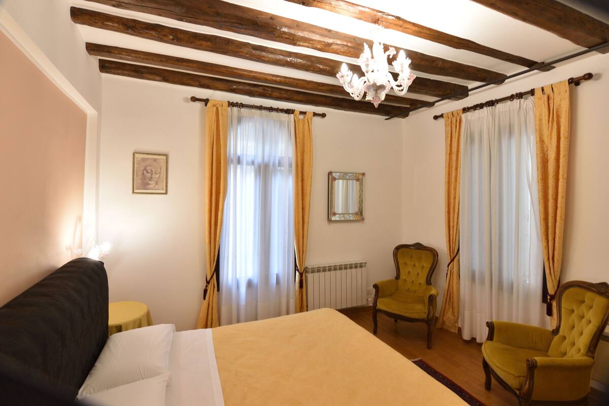 A room with a bed, two chairs, a chandelier, and curtains.