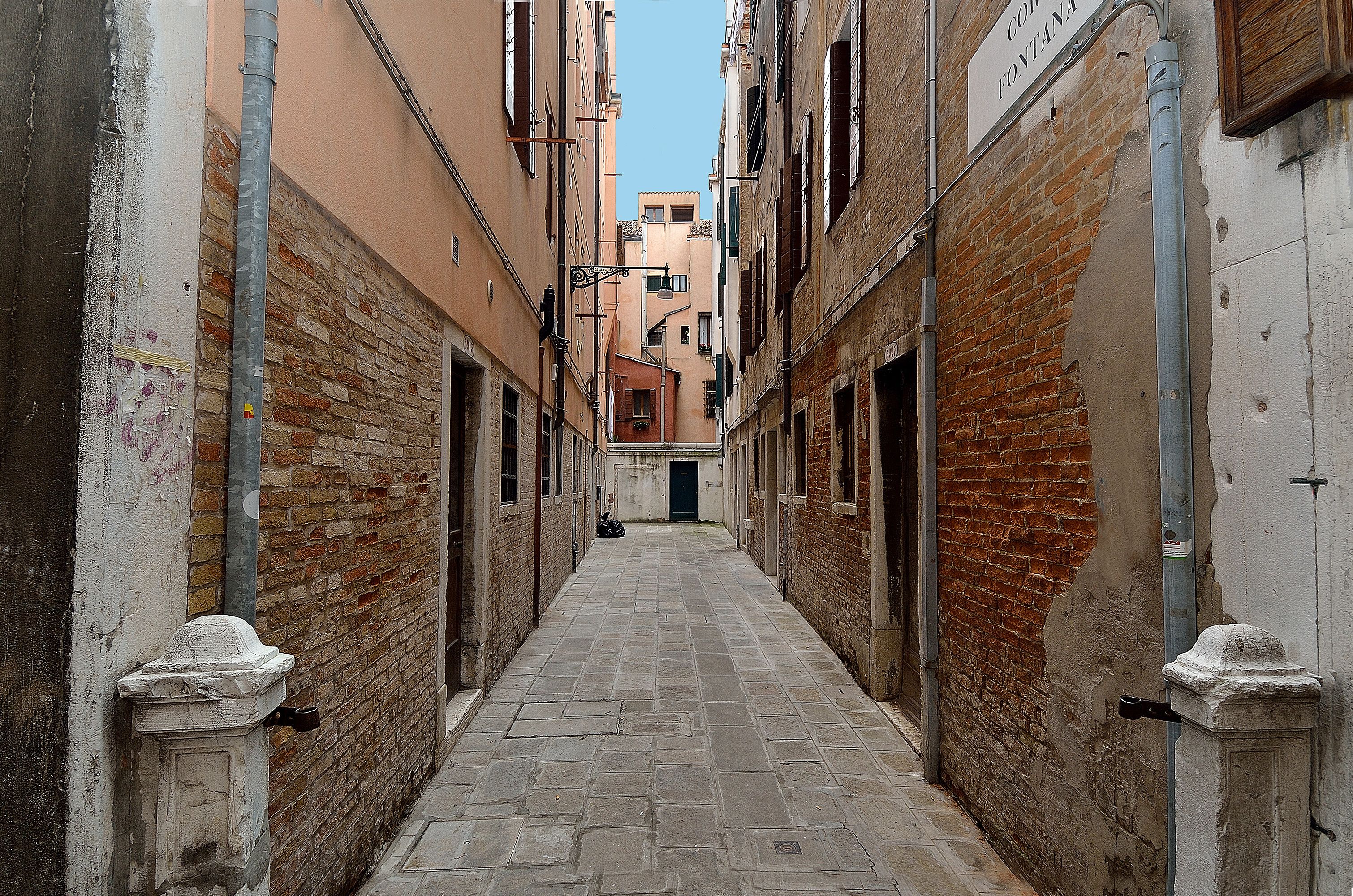 A narrow alleyway with brick walls and a stone pavement.