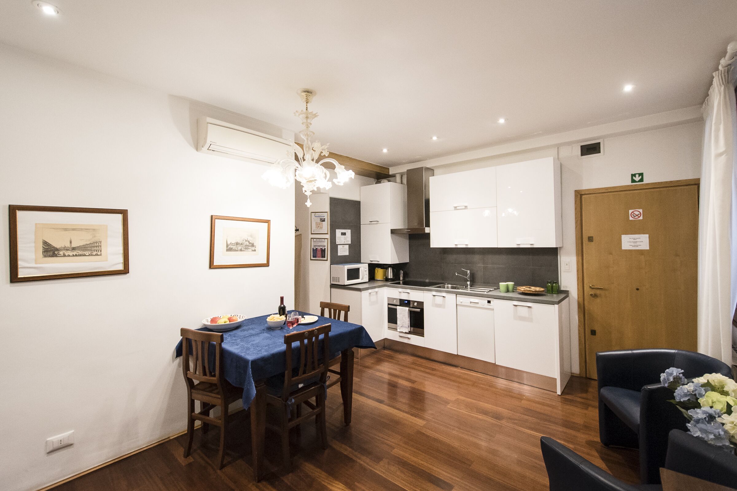 A modern kitchen with white cabinets, a dining table with chairs, and a chandelier.