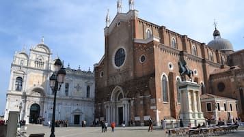 Una plaza histórica con una iglesia grande que tiene una cúpula y estatuas, rodeada de turistas y mesas al aire libre.