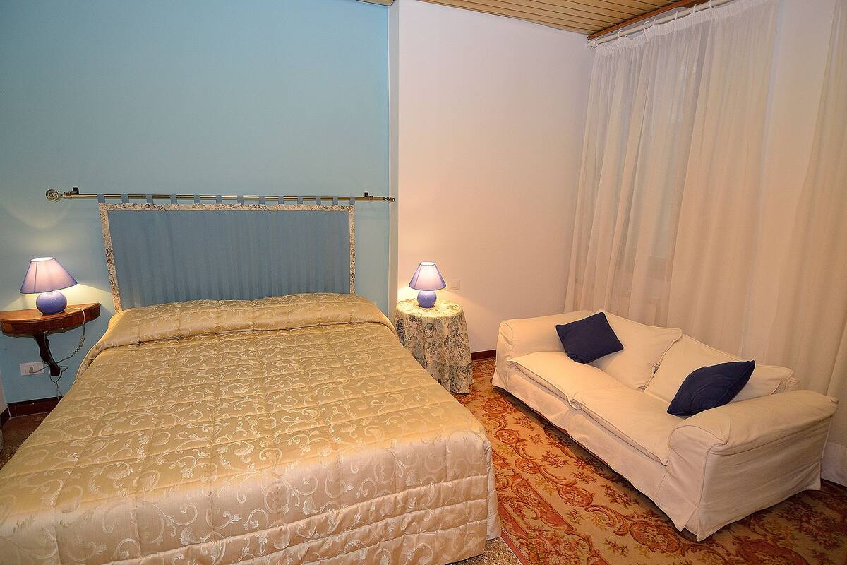 A hotel room with a bed, a white sofa, two lamps, and a curtain.