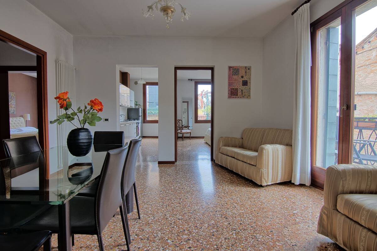 A spacious living area with a glass dining table, a sofa, and a TV in the background.