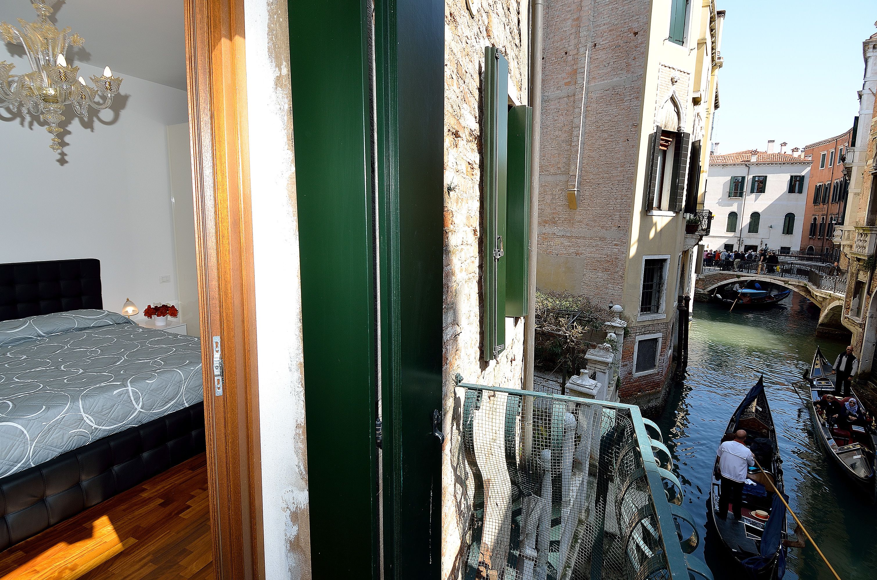 A narrow Venetian canal with gondolas, a bed with a patterned bedspread, and a chandelier.