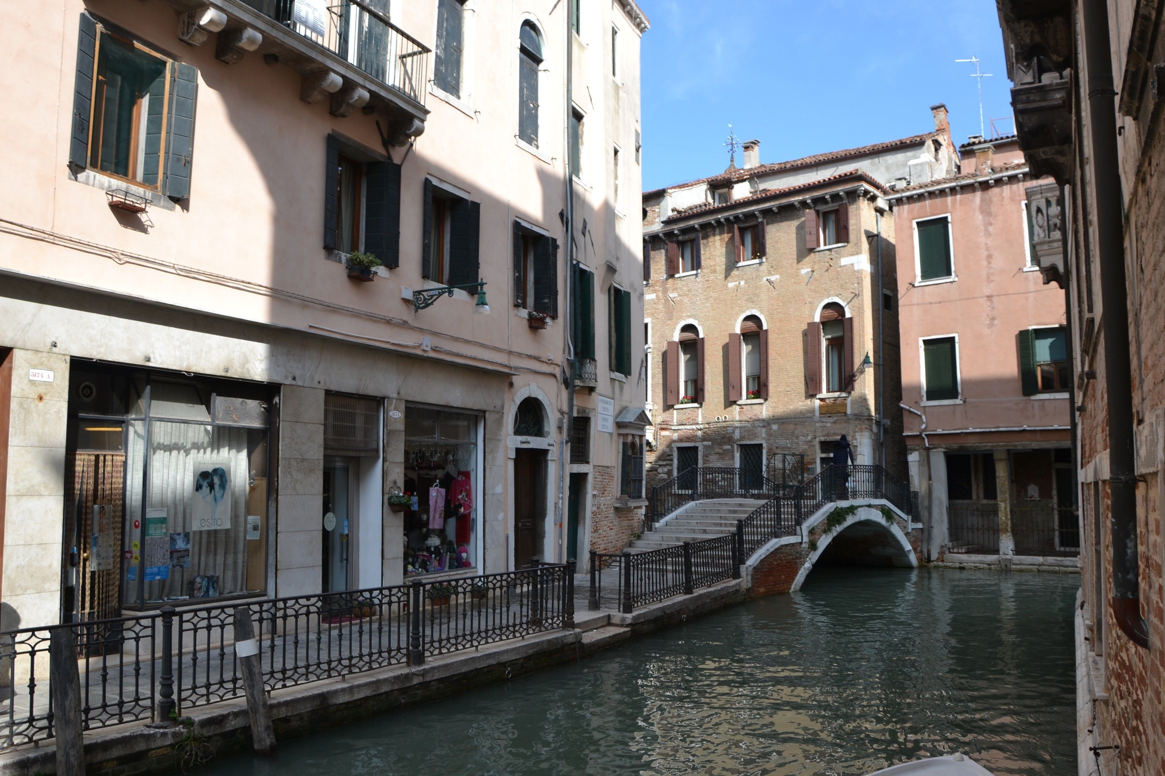 A canal with buildings on either side, a bridge, and a shop with a sign that reads "OSIO".