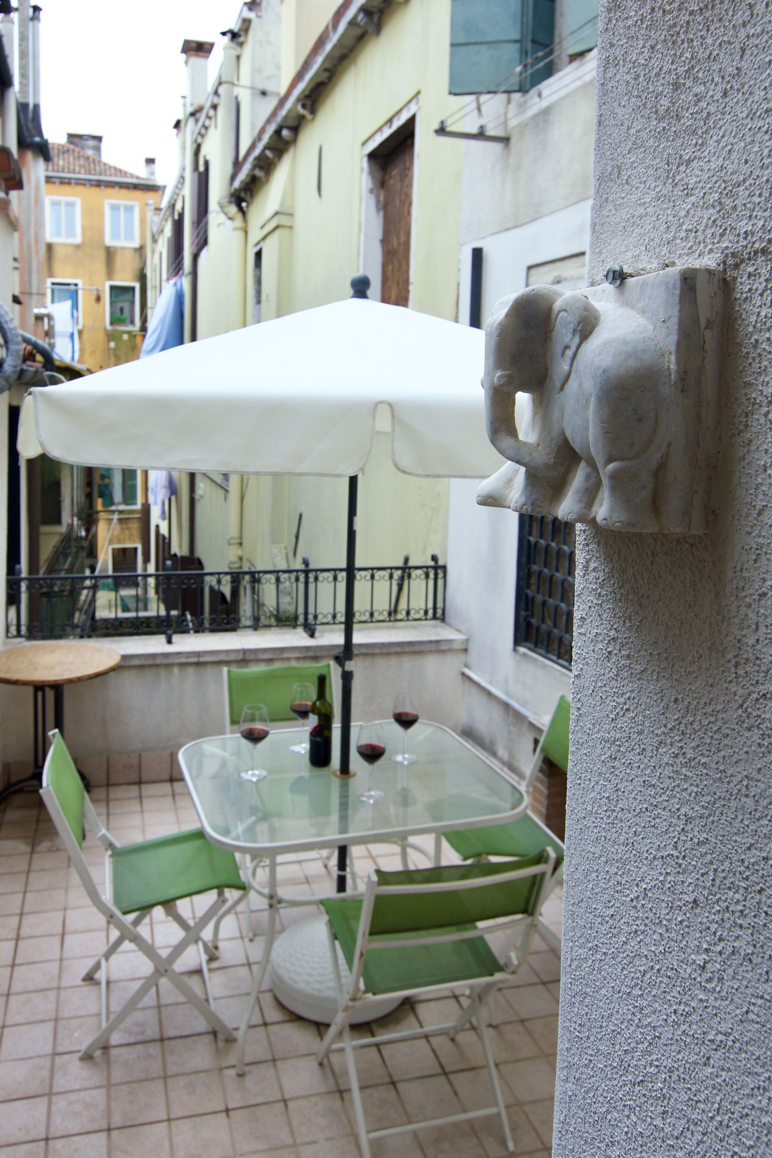 Eine Außenpatio mit Tisch und Stühlen, einem weißen Sonnenschirm und einer dekorativen Steinelefant.