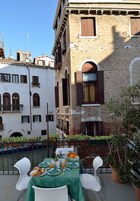 Una terrazza con tavolo apparecchiato per la colazione, affacciata su un canale ed edifici storici.