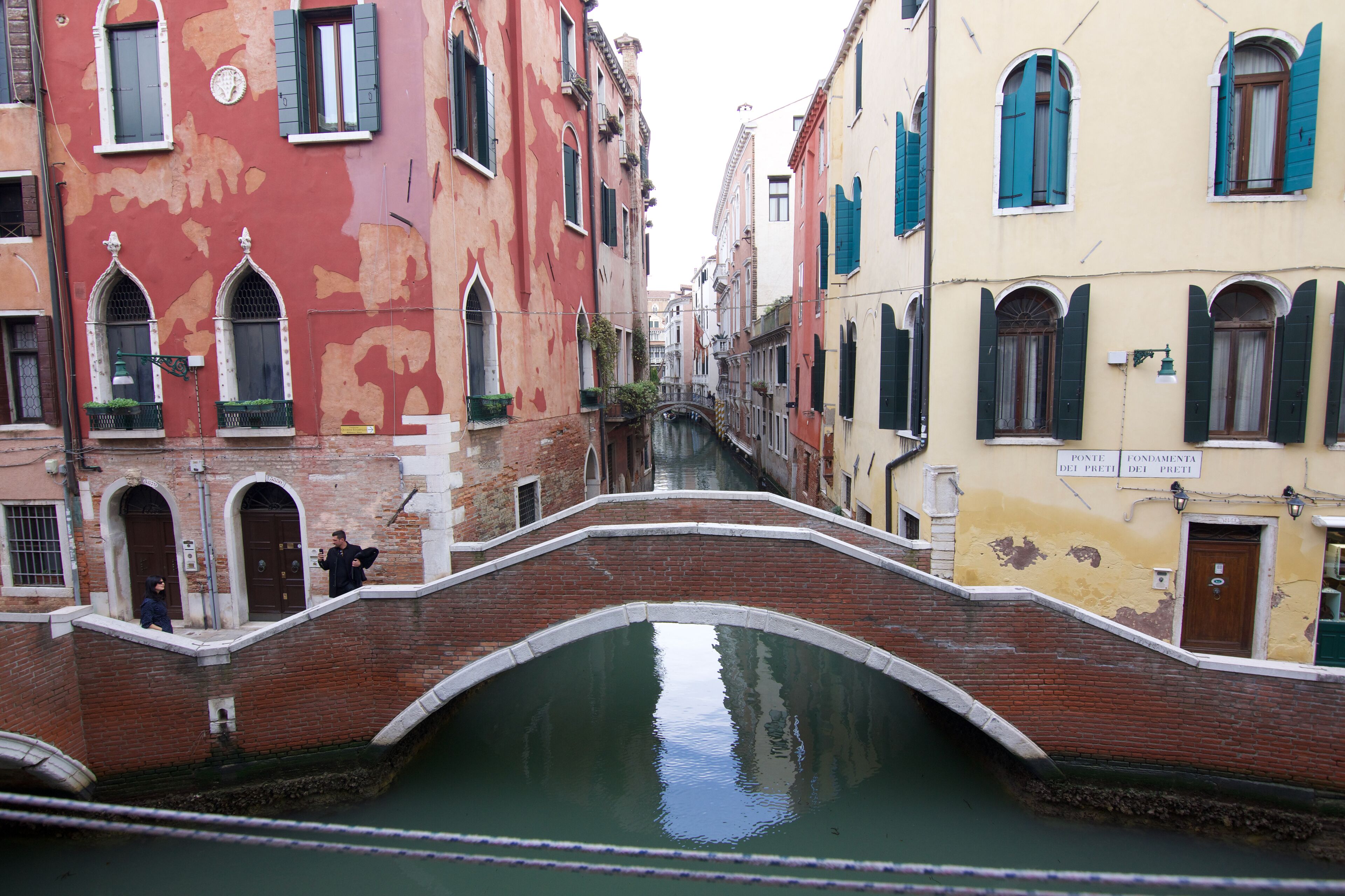 A canal with a bridge, buildings with arched windows, and a sign that reads "Ponte del Preti".