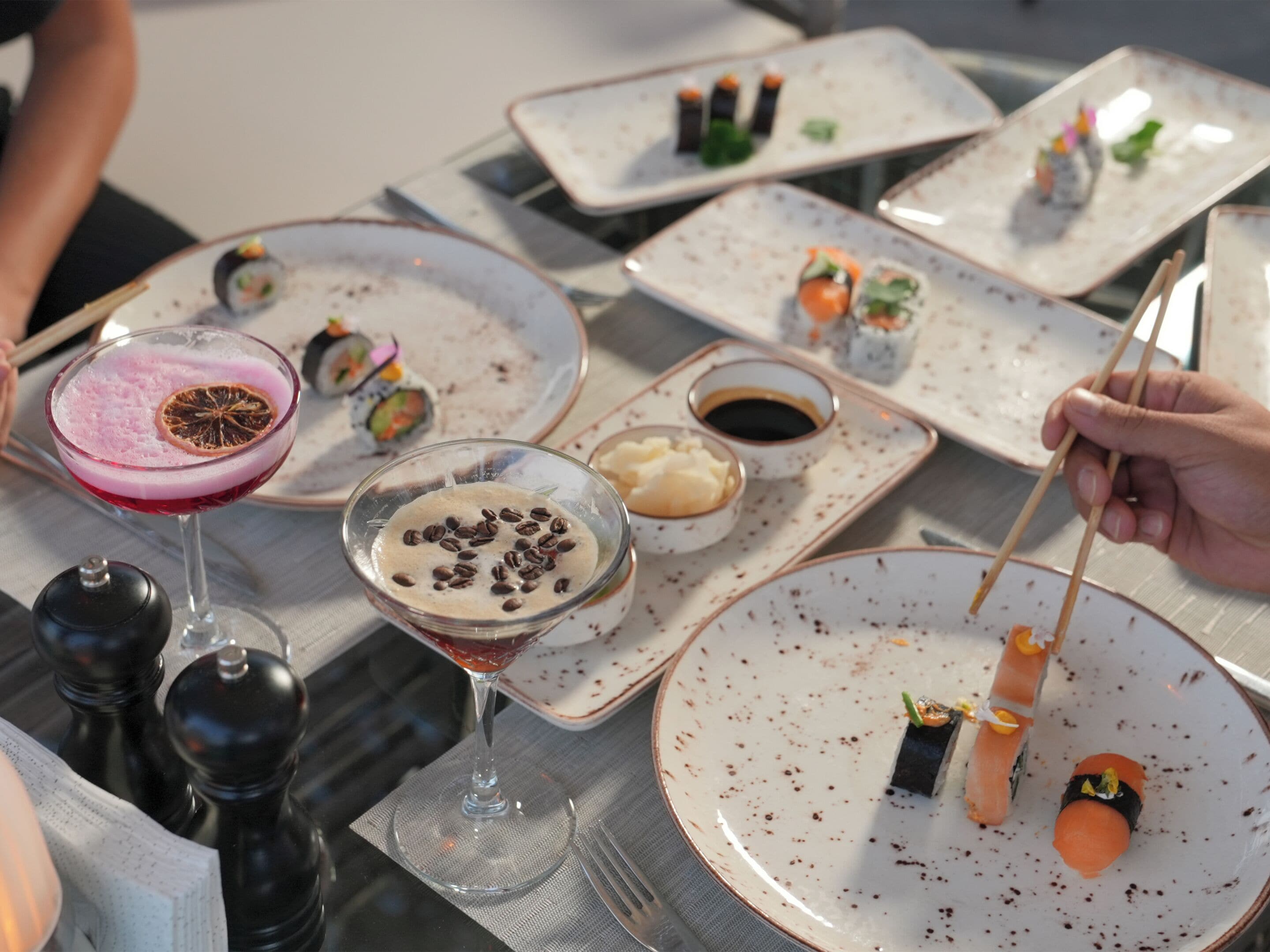Une table où l’on voit différents plats, notamment des sushis, ainsi qu’un verre à martini contenant une boisson rose.