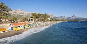 A beach with boats, umbrellas, and a mountain backdrop. - Crystal Aura Aqua Collection (Kemer)