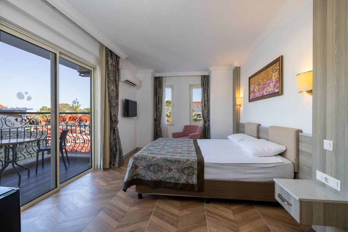 A hotel room with a bed, a chair, a TV, and a balcony with a table and chairs.