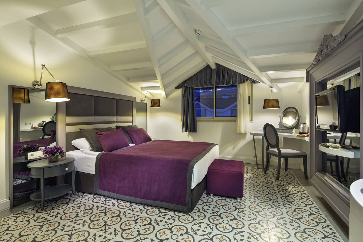 A bedroom with a large bed, a desk, and a mirror.