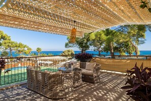 Un área de estar al aire libre techada, con mobiliario de mimbre, una piscina y vistas al mar.