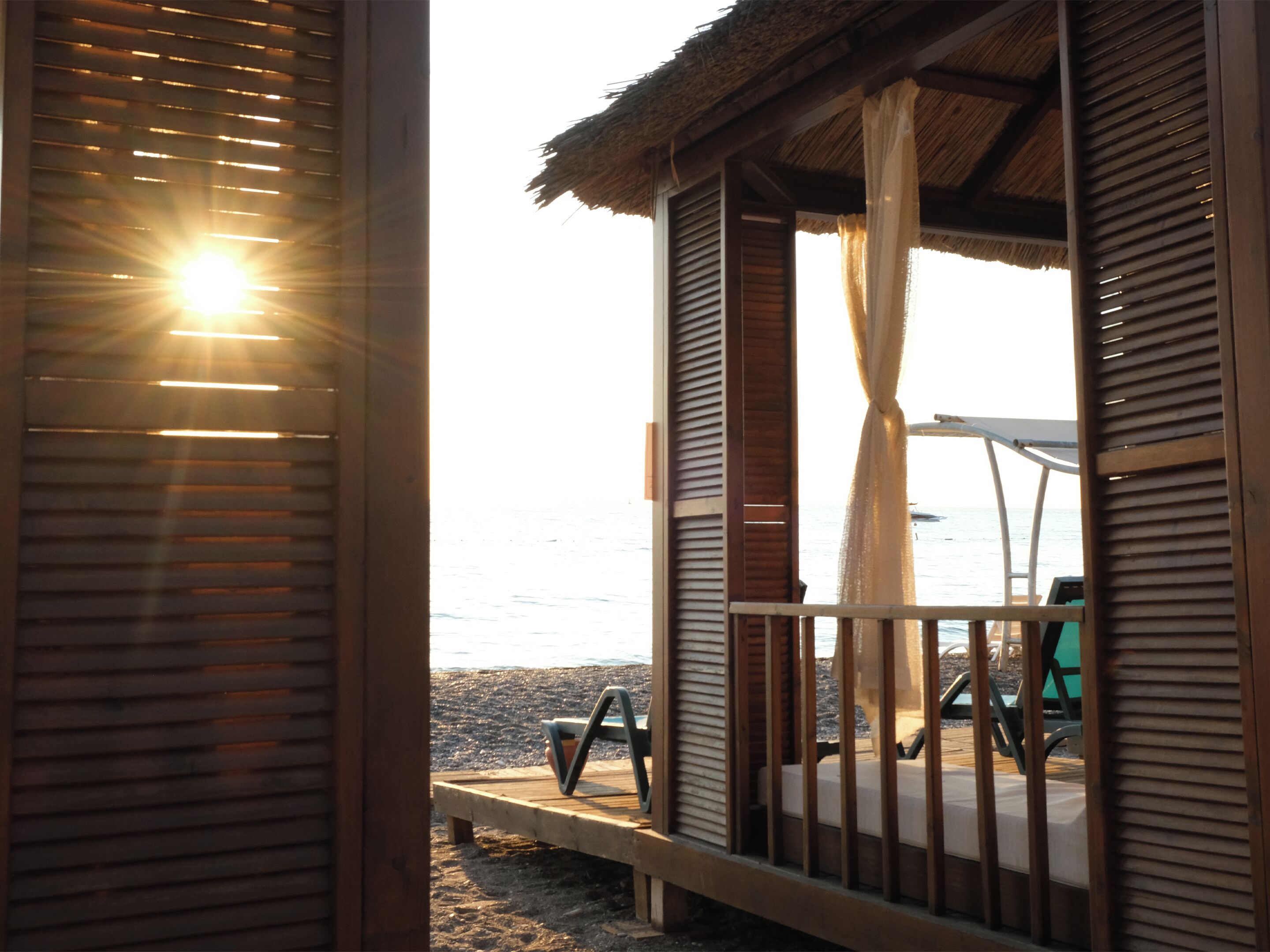 A beachside hut with a thatched roof, a wooden bench, and a view of the sea.
