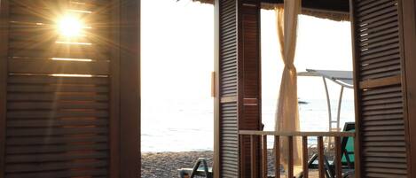 A beachside hut with a thatched roof, a wooden bench, and a view of the sea.