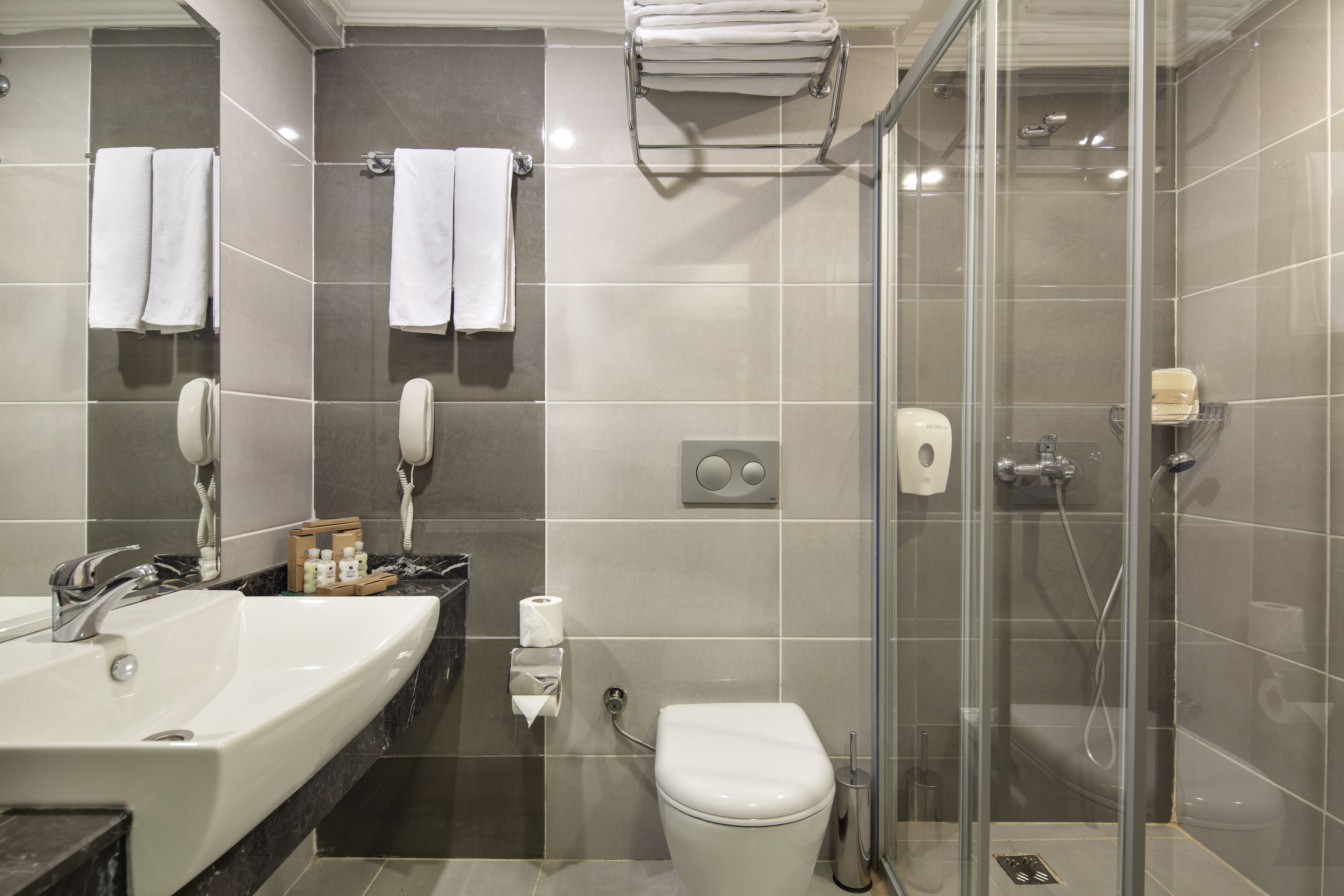 A modern bathroom with a sink, mirror, towel rack, toilet, and glass-enclosed shower.