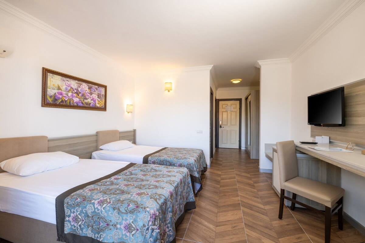 A hotel room with two beds, a desk with a chair, a television, and a hallway leading to another room.