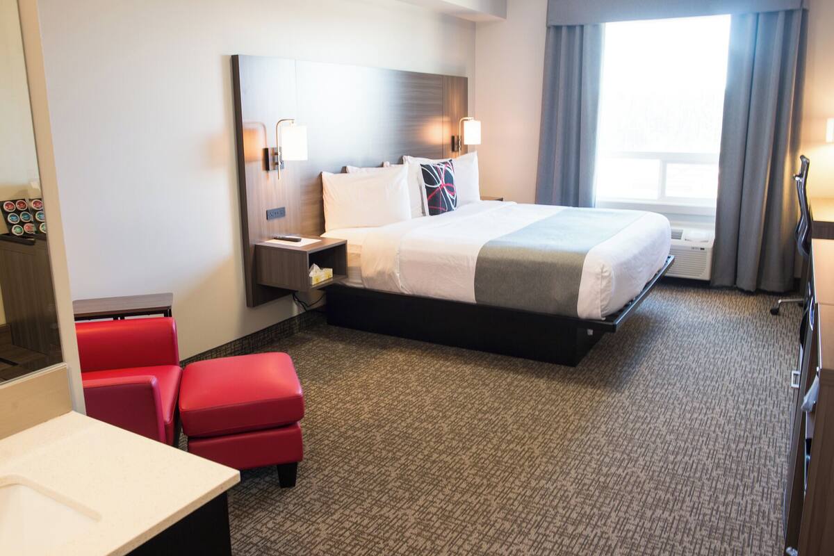 A hotel room with a large bed, a desk, a red chair, and a window with curtains.