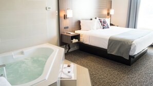 Een hotelkamer met een groot bed, een aparte badkamer met badkuip, en een nachtkastje met lamp en telefoon.