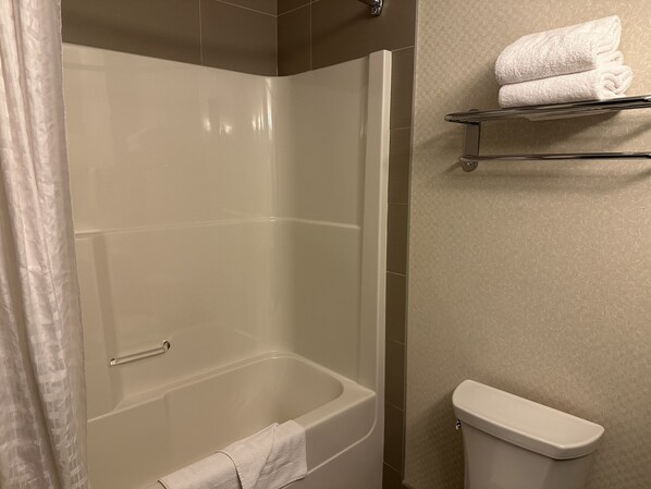A bathroom with a glass-enclosed shower, a toilet, and a towel rack with folded towels.