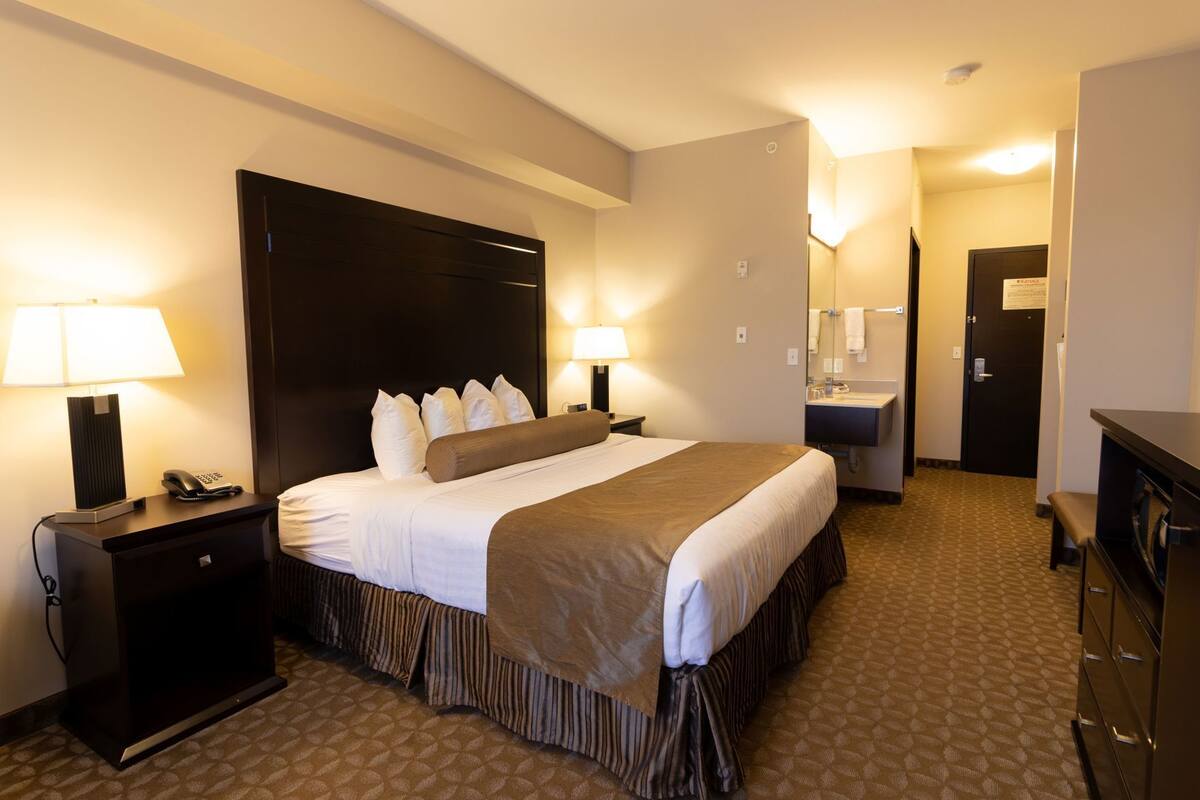 A hotel room with a large bed, bedside lamps, a desk with a phone, a mirror, and a bathroom with a sink and towel rack.
