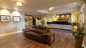 Een lobby met een bruine leren bank, houten vloeren, ingelijste foto’s aan de muur, een receptiebalie en een grote bloemstelling.