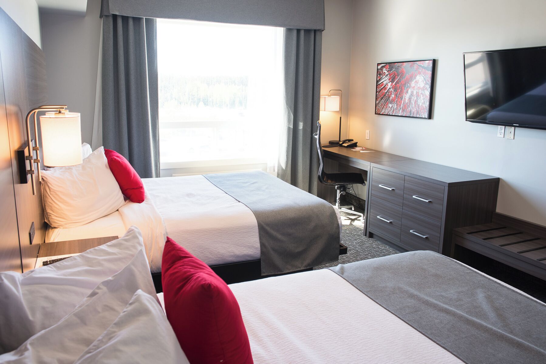 Habitación de hotel con dos camas, un escritorio, una silla, un televisor y una ventana con cortinas.