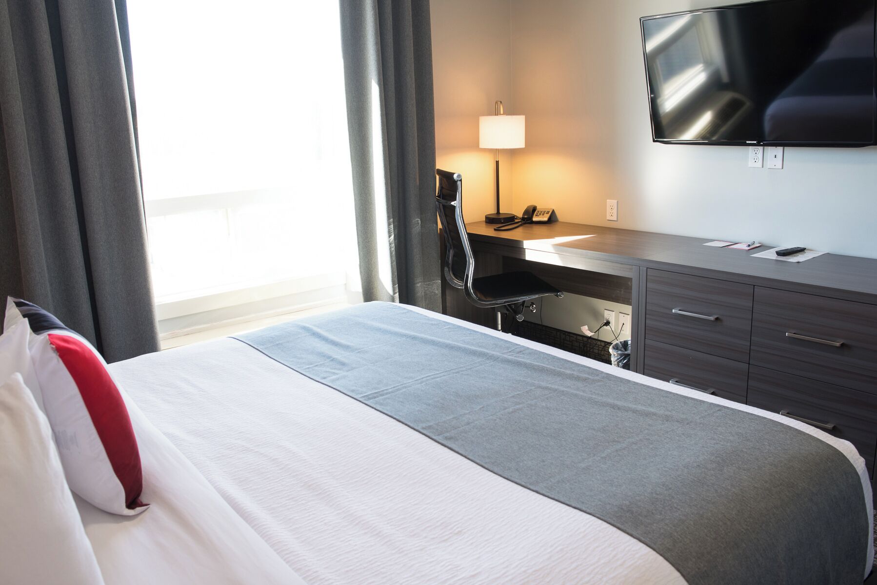 A hotel room with a bed, a desk, a chair, a TV, and a lamp.