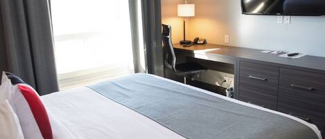 A hotel room with a bed, a desk, a chair, a TV, and a lamp.