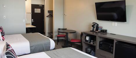 A hotel room with two beds, a desk with a coffee maker, a TV, and a microwave.