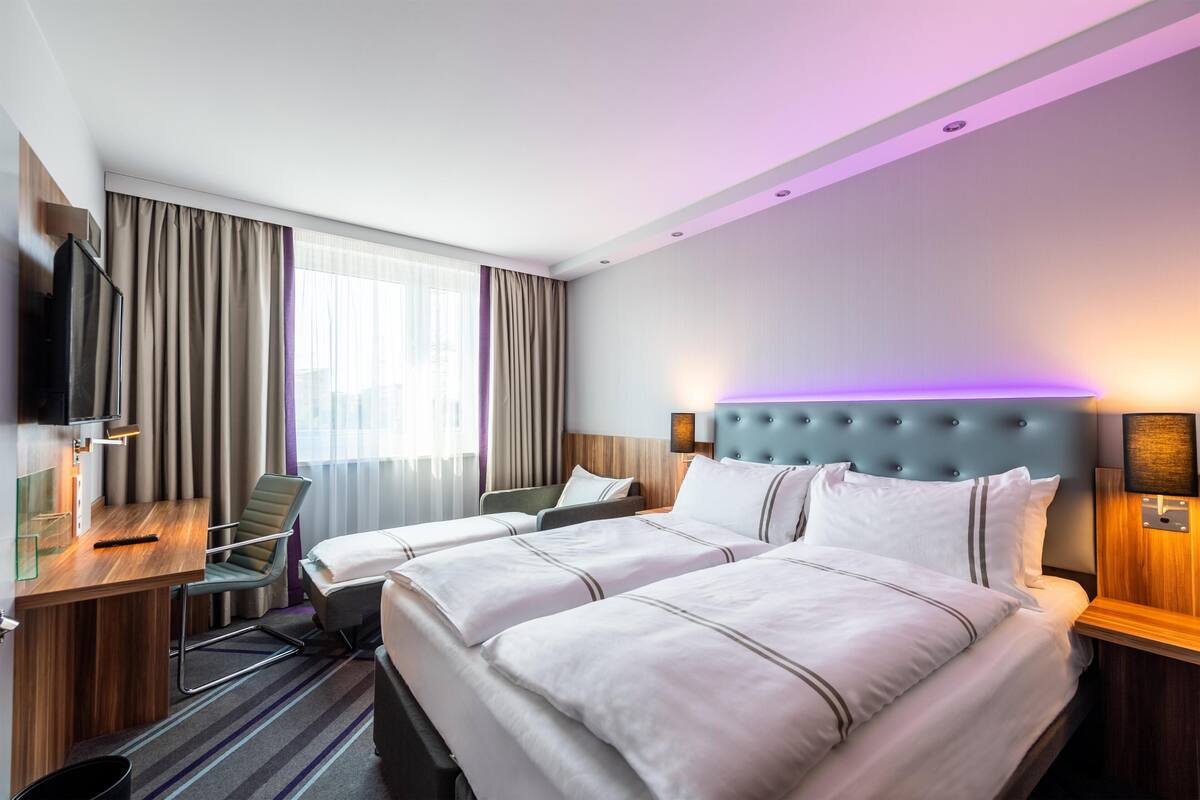 A hotel room with two beds, a desk, a television, and a window with curtains.