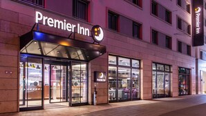 Een gevel van een Premier Inn hotel met een duidelijke ingang, grote ramen en een fietspad langs de stoep.