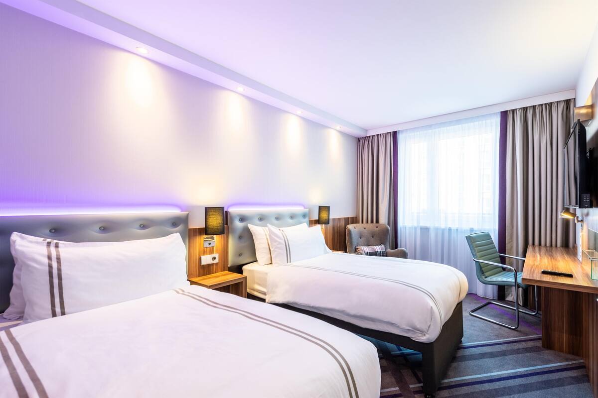 A hotel room with two beds, a desk, a chair, a TV, and a window with curtains.