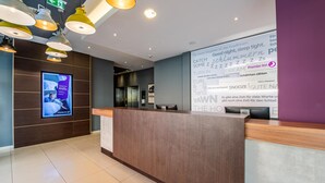 Een hotel receptie met een houten receptiebalie, een scherm met de naam van het hotel en een muur met tekst en symbolen.