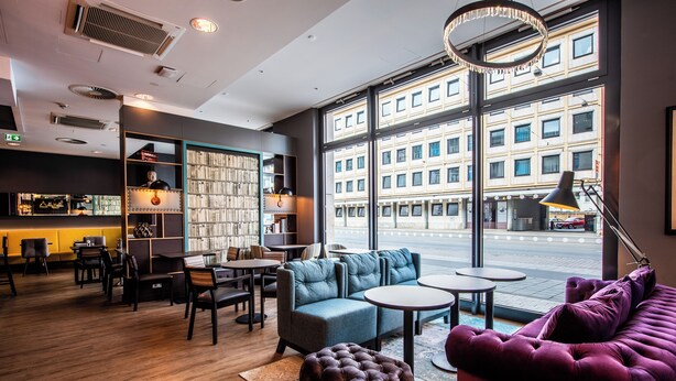Een modern interieur met een zithoek, boekenkasten en grote ramen met uitzicht op een stadsgezicht.