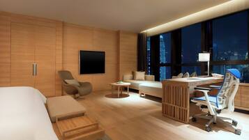 A modern hotel room with a bed, a desk, a chair, a sofa, and a large window with a city view.