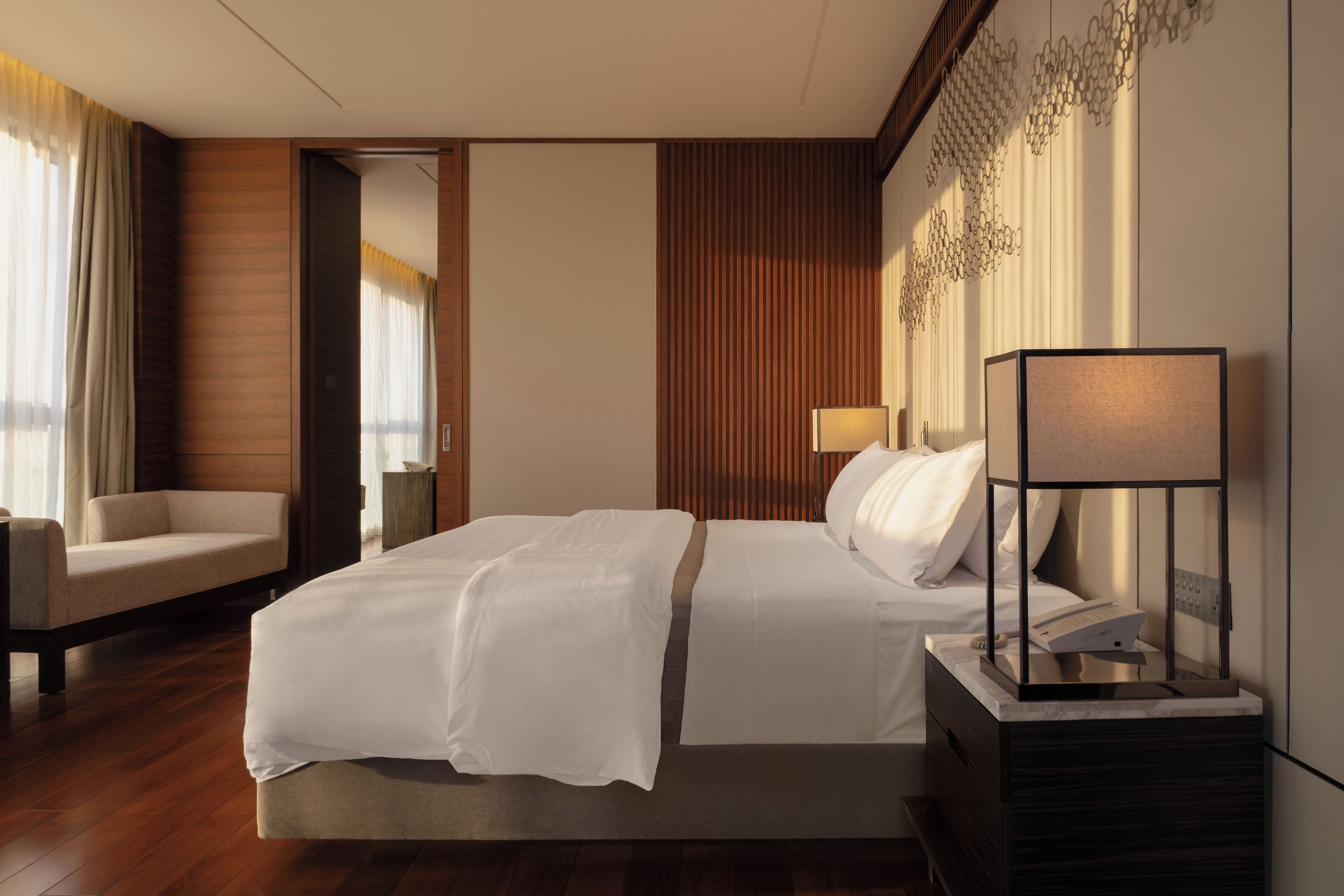 A hotel room with a large bed, a bedside table with a lamp, a chair, and a wooden floor.