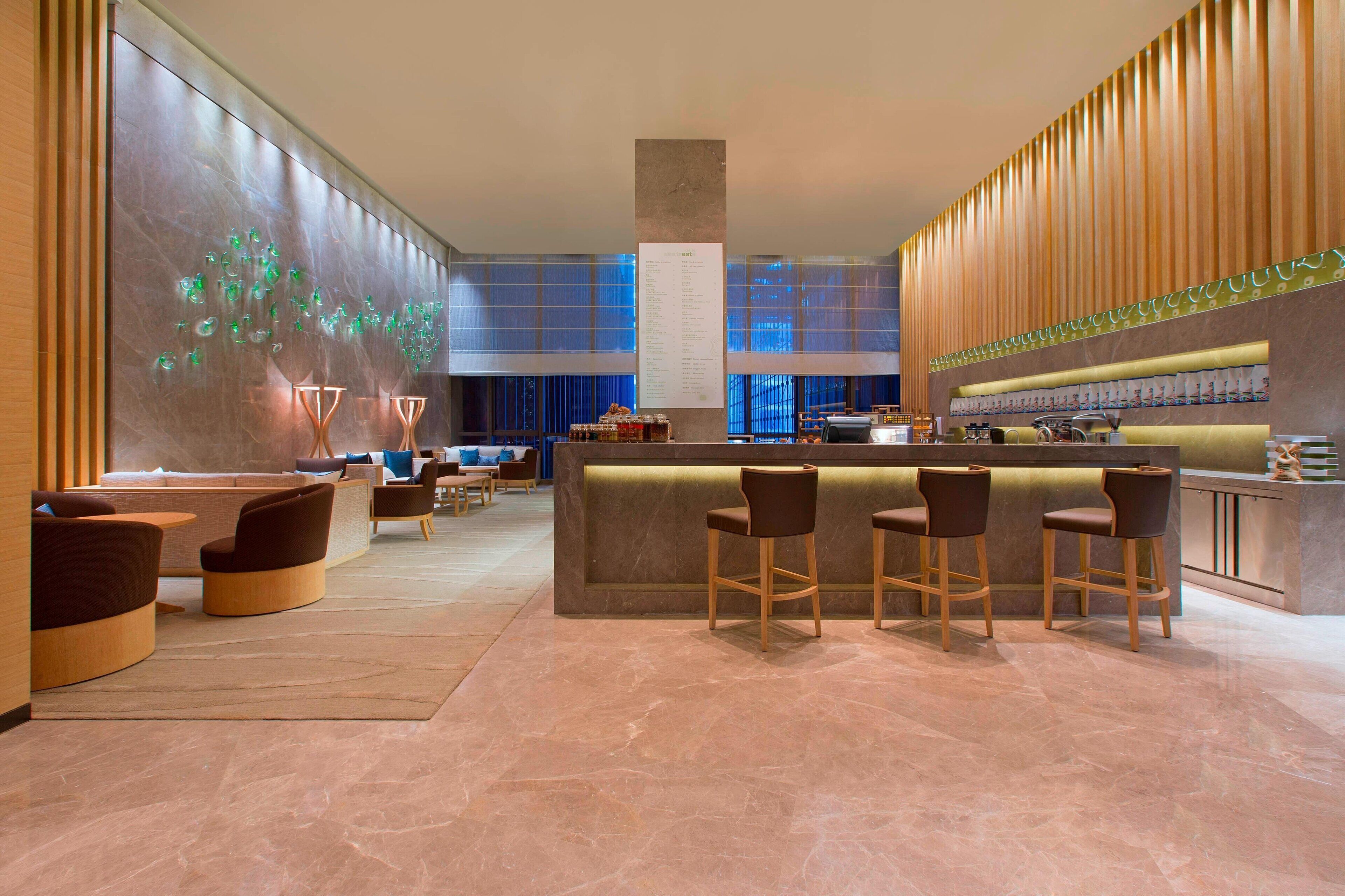 Un moderno vestíbulo de hotel con zona de bar, asientos y una pared decorativa.