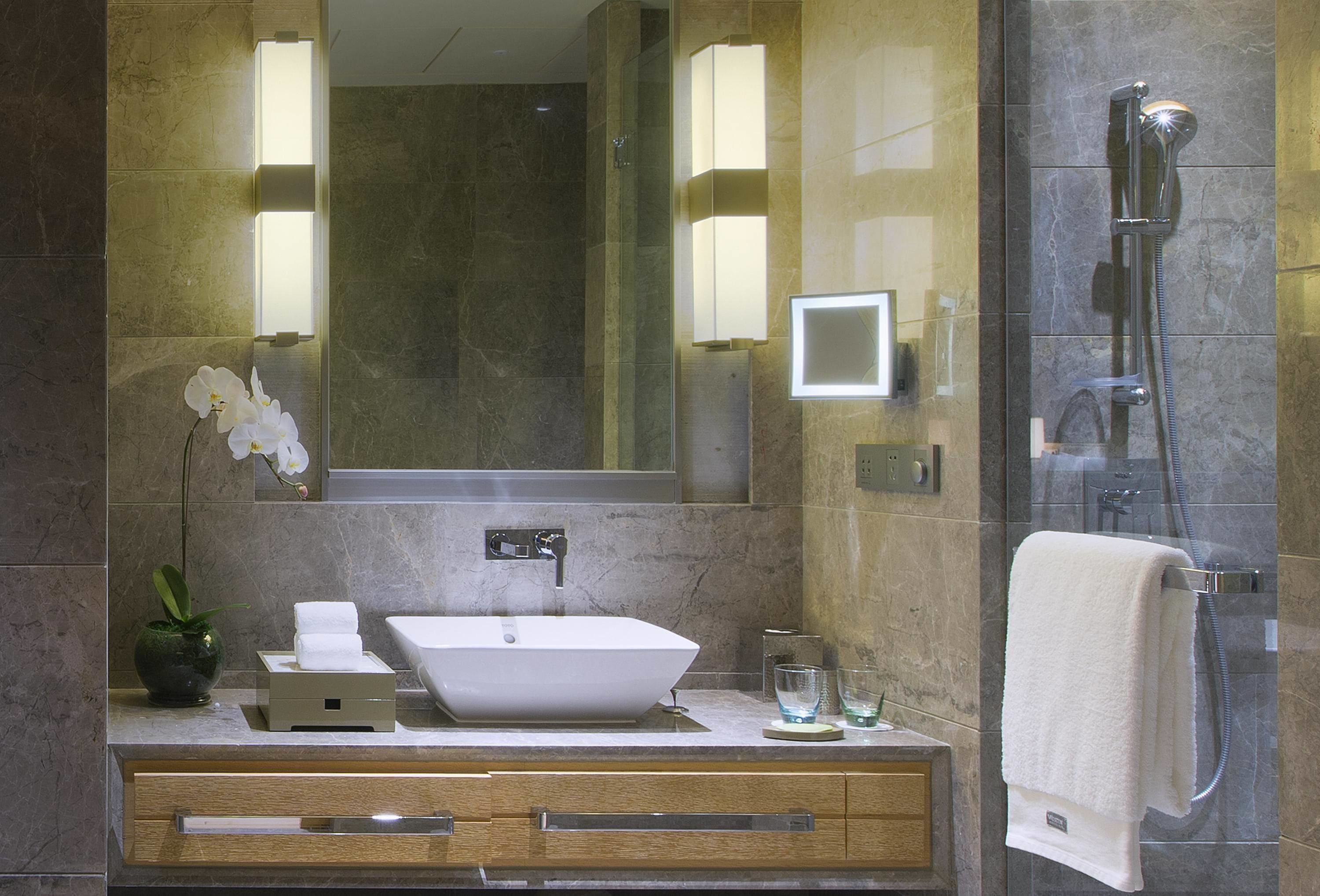 A modern bathroom with a large mirror, a vessel sink, a shower, and a towel rack.