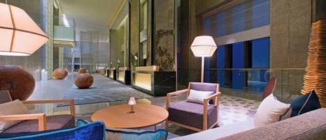 A spacious lobby with modern furniture, including sofas and chairs, a round table, and a large floor lamp.