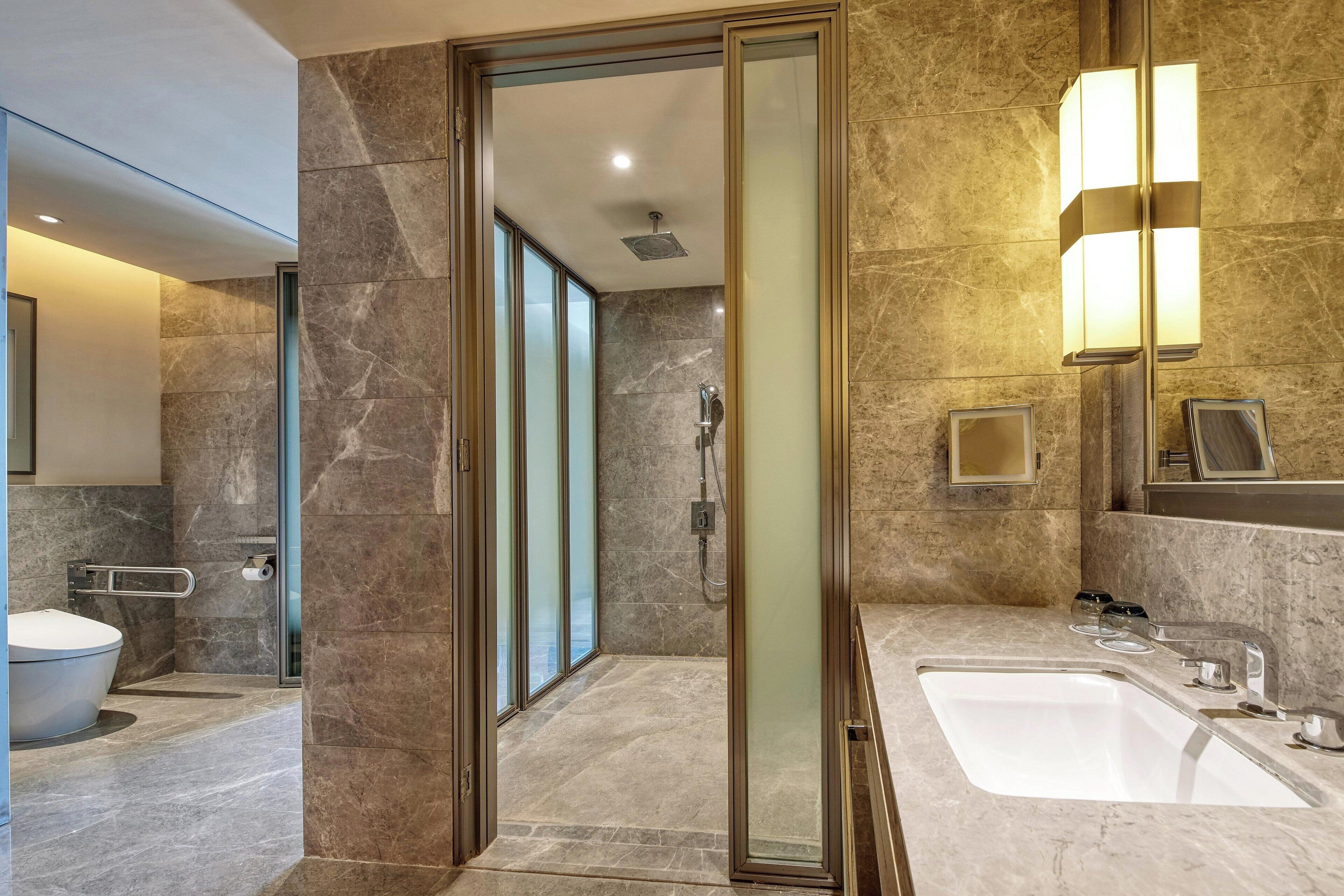 A modern bathroom with a glass-enclosed shower, a large sink, and a mirror with integrated lighting.