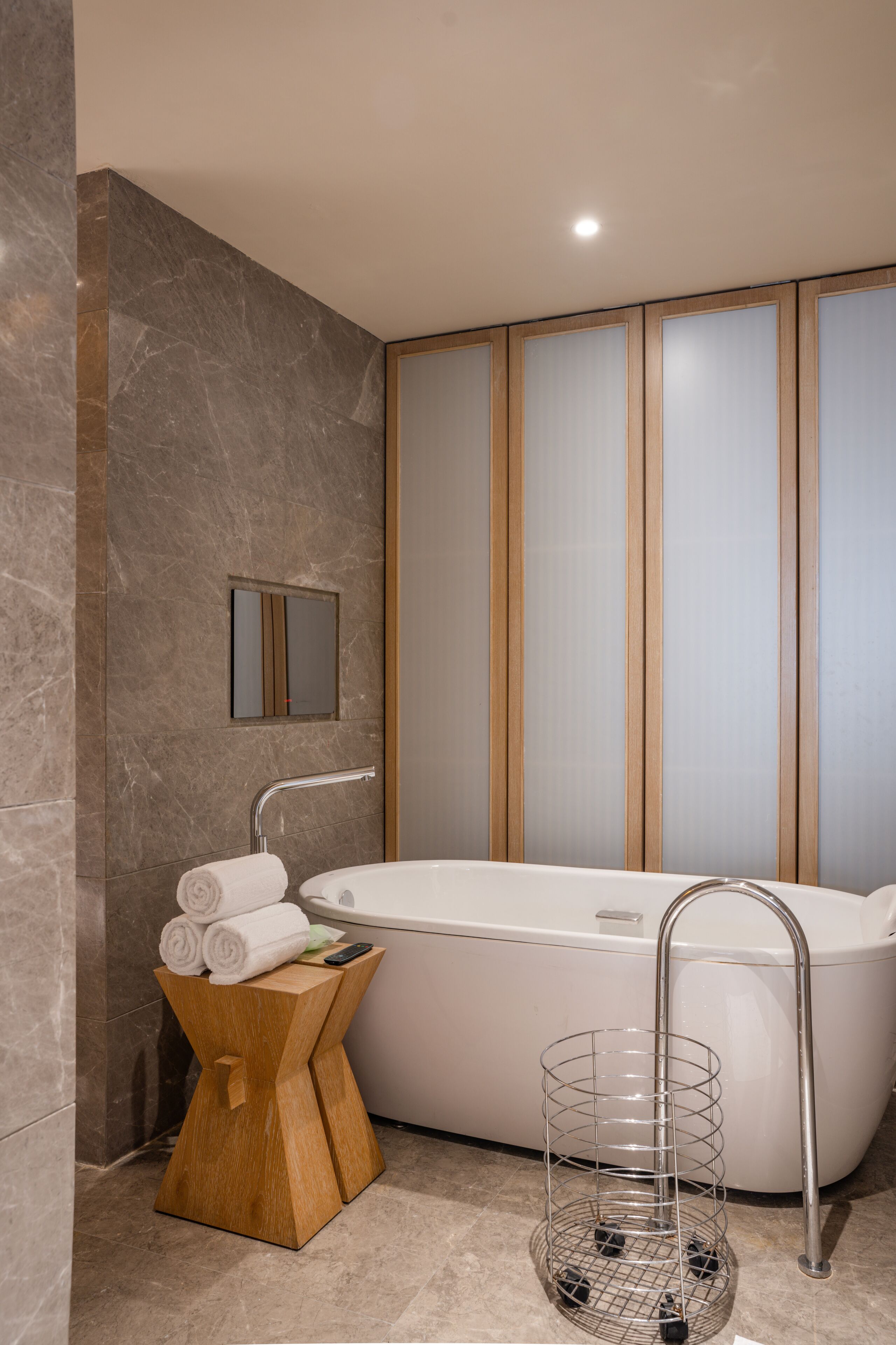 A modern bathroom with a freestanding bathtub, a wooden side table with towels, and a metal towel rack.