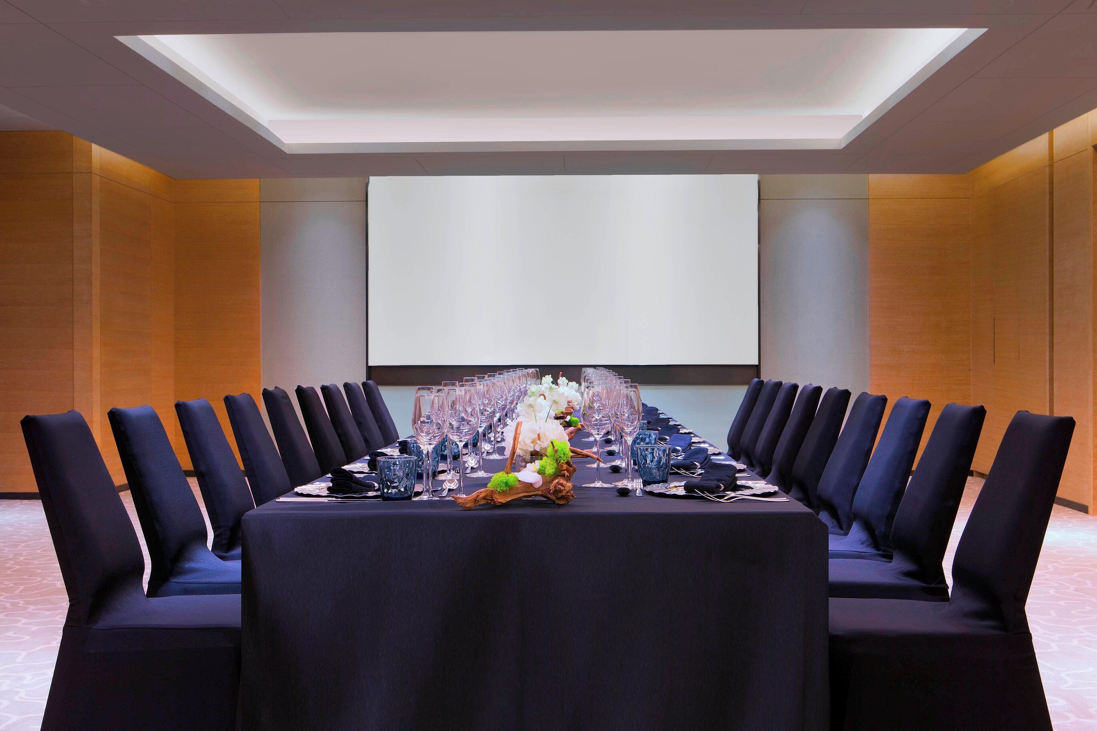 A conference room with a long table, chairs, and a projector screen.