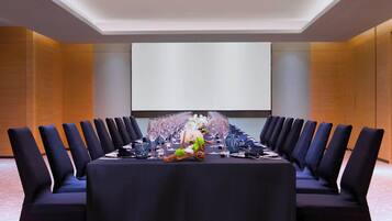 A conference room with a long table, chairs, and a projector screen.