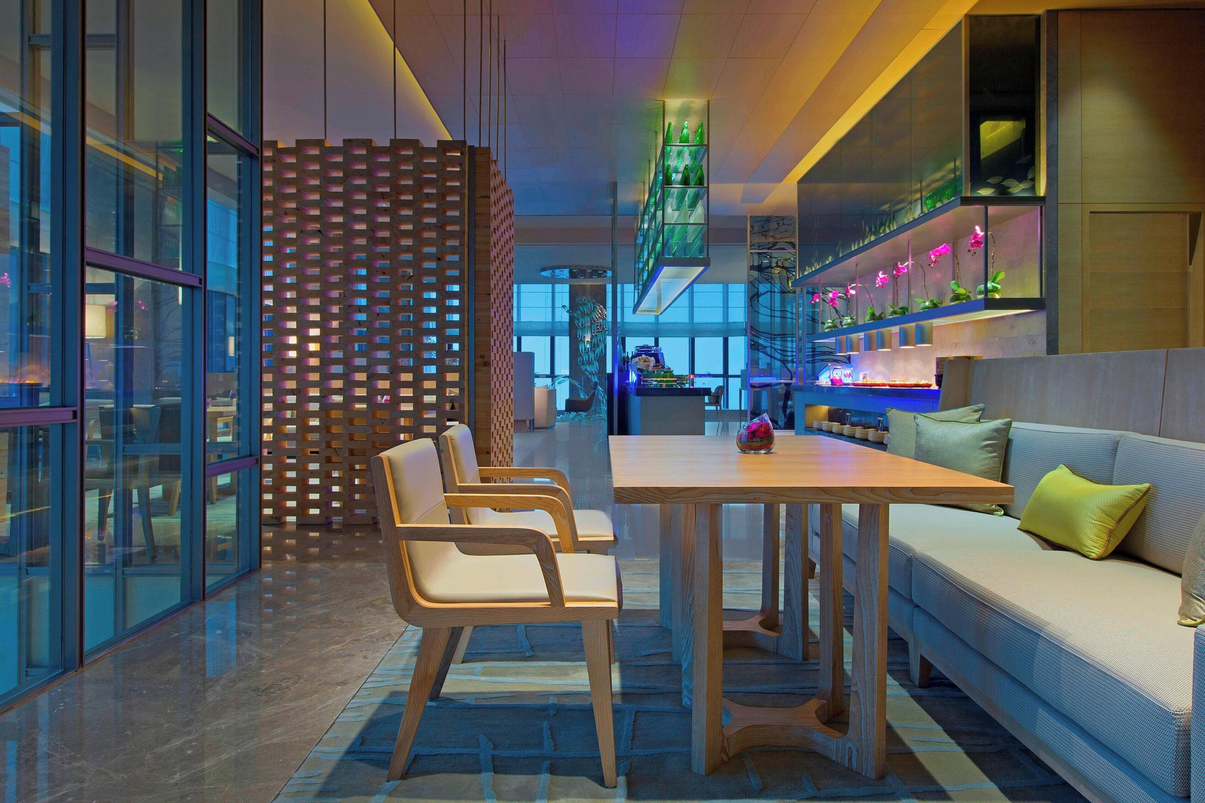 A modern interior with a wooden table and chairs, a sofa with cushions, and a decorative wall with shelves.