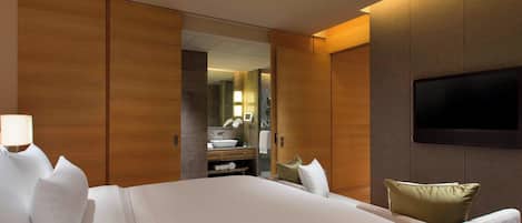 A hotel room with a large bed, a TV mounted on the wall, and a bathroom visible through an open door.